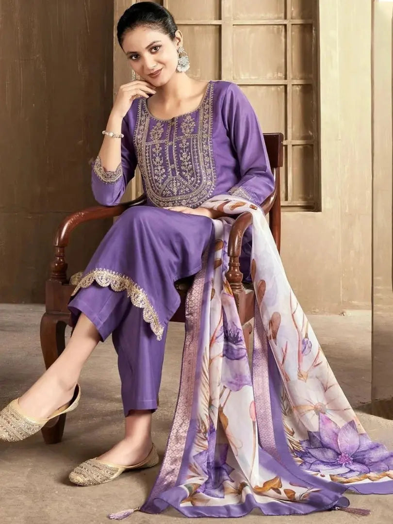 Woman in a purple traditional outfit with a floral scarf, sitting on a wooden chair.